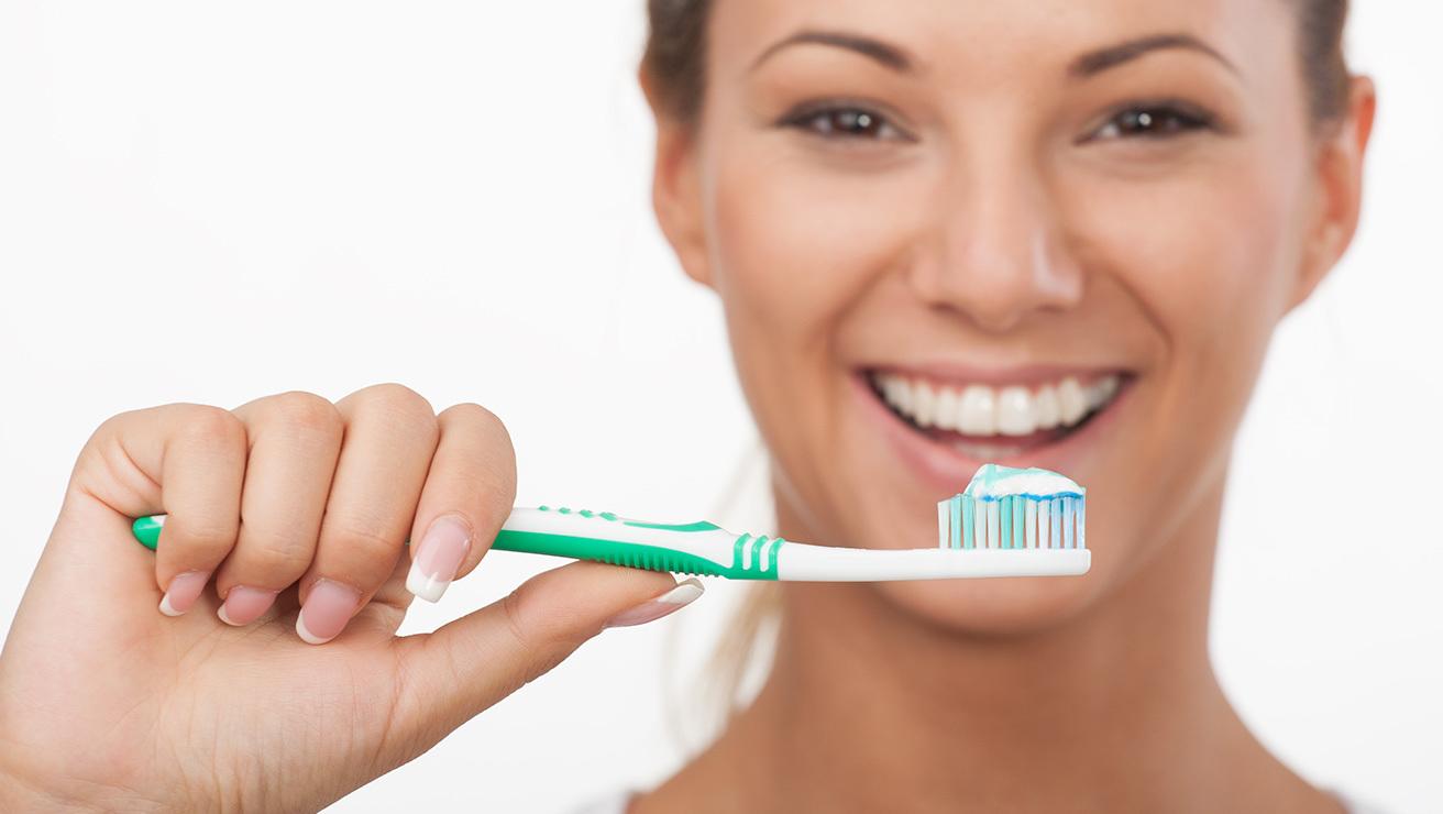 una mujer que sostiene un cepillo de dientes y dentífrico